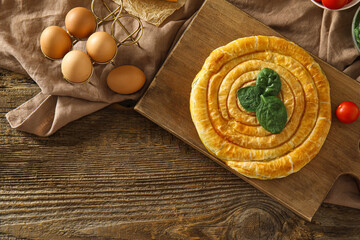 Board with tasty spinach pie and ingredients on wooden background
