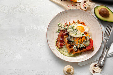 Delicious Belgian waffles with bacon, egg and vegetables in plate on light background