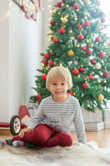 Beautiful toddler child, sitting in front of  Christmas tree, decoration around him