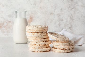 Fototapeta na wymiar Crunchy rice crackers and bottle of milk on light background