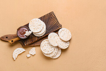 Board with corn crackers and melted chocolate on color background