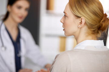 Fototapeta premium Friendly smiling female doctor and patient woman discussing current health examination in sunny clinic. Perfect medical service in hospital. Medicine concept