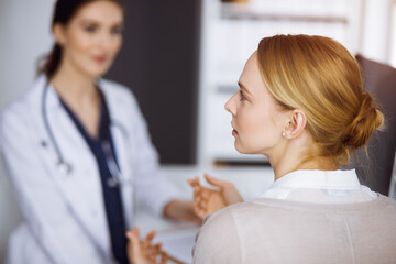 Obraz premium Friendly smiling female doctor and patient woman discussing current health examination in sunny clinic. Perfect medical service in hospital. Medicine concept