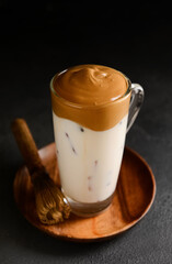 Glass cup of tasty dalgona hojicha latte and chasen on dark background