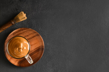 Glass cup of tasty dalgona hojicha latte and chasen on dark background