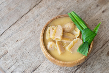 Banana in coconut milk, Thai dessert in wooden bowl with pandan leaf on wooden background.