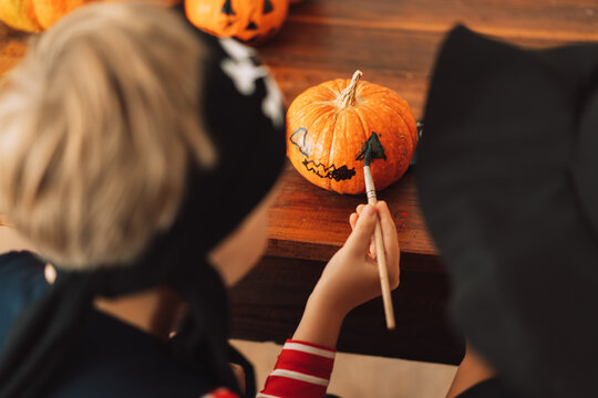 Children in witch and pirate costumes paint face on pumpkin.