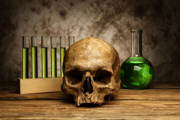 Human skull with laboratory glassware on table against dark background