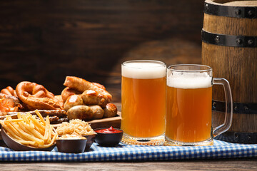 Mugs of cold beer, wooden board with Bavarian sausages and snacks on table. Oktoberfest celebration