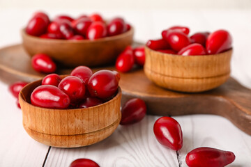 Bowls with ripe red dogwood berries on light wooden background, closeup