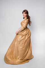 Fototapeta premium A full-length portrait of a girl in a golden rococo gown posing isolated on a white background.