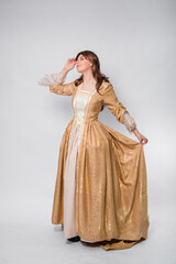 Fototapeta premium A full-length portrait of a girl in a golden rococo gown posing isolated on a white background.