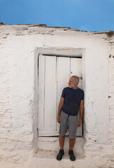 Fototapeta na wymiar Adult man against white wooden door and white wall with blue sky