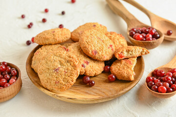 Wooden plate with tasty cranberry cookies and berries on light background