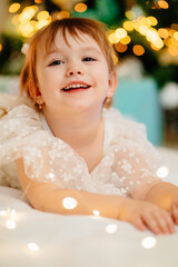 a cute girl lies under the Christmas tree and plays with a garland