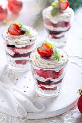 Dessert with red sponge cake, currant jam and cream, garnished with kaleunik in glass glasses, selective focus. The concept of a dessert for the holiday.