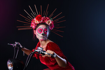 Young woman with painted skull on her face and motorcycle against dark background. Halloween celebration