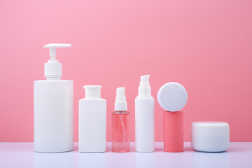 Set of beauty products in a row on white table against pink background
