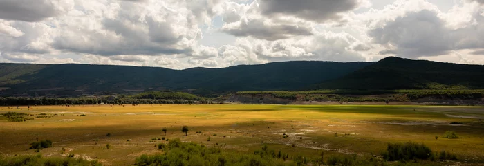 Foto op Canvas Panoramic landscape of plain with mountains in the background and cloudy sky with dramatic light © Carlos Cairo