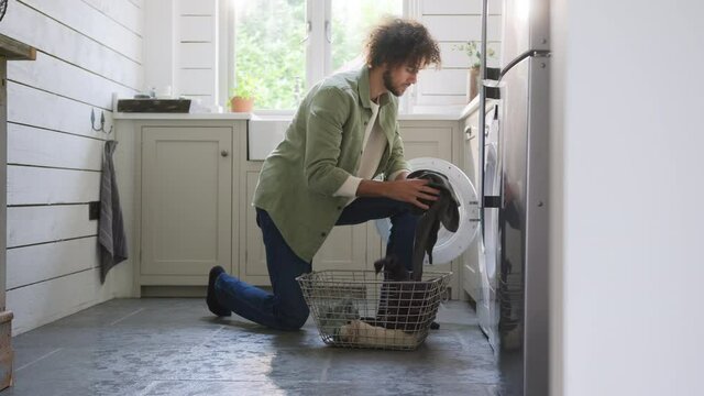 Slow motion of man loading washing machine in kitchen