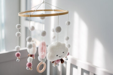 Baby crib mobile with smiling clouds and snow. Kids handmade toys above the newborn crib. First baby eco-friendly toys made from felt and wood hanging in light room
