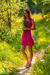 Naklejka na ściany i meble Portrait of a slender young happy smiling woman with a bouquet of field flowers in summer on a sunny day in nature