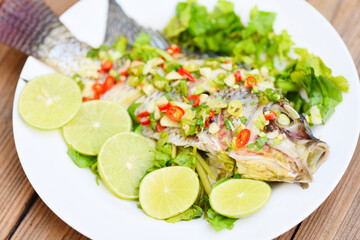 Steamed tilapia fish with chili and lime lemon sauce with herb and Vegetable on plate, Food cooked tilapia fish steam lime - Thai food