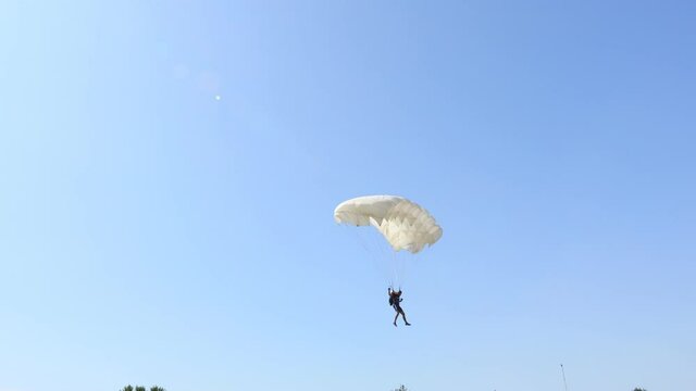 Parachutist with an open parachute is flying and slows down for landing on ground. Skydiving, gliding, parachute jump.