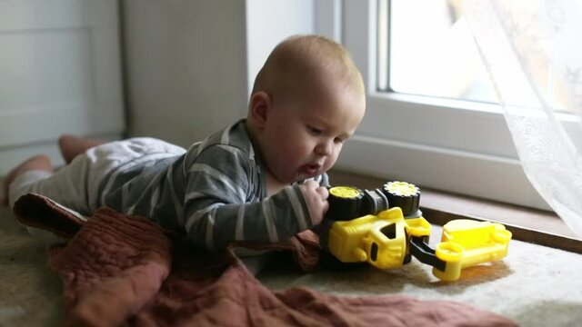 Cute caucasian baby learning to crawl and play on the floor with a plastic yellow tractor, toddler 5 6 months on the stomach on the floor, children development, subject manipulative activity