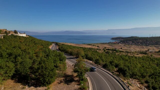 Car driving on curved road toward blue lake in panoramic landscape of Albania