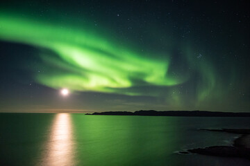 Fototapeta na wymiar Bright green nortern lights on the shore of Baltic sea in Teriberka