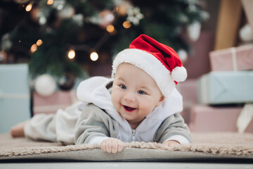 Adorable baby in red Santa hat on floor.