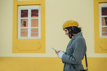 Woman using smartphone and wearing yellow beret and a gray coat