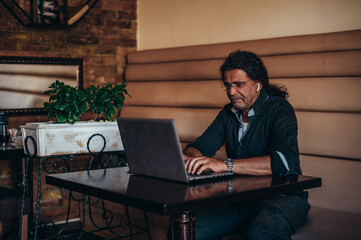 Senior hispanic cuban men using laptop while working remotely in a cafe