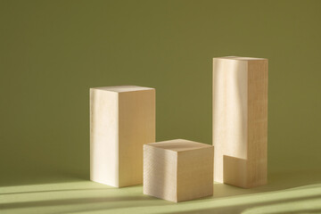 Square stands made of wood of different heights on green background in rays of sunlight. Concept of 3d podium for presentation of cosmetic products, demonstration of goods