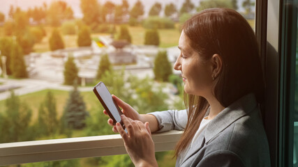 Fototapeta premium woman in business suit typing on the phone by the open window.