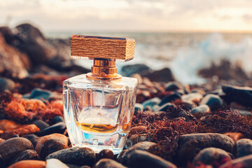 A golden transparent perfume bottle with drops on a wet pebble beach. Close-up. In the background,...