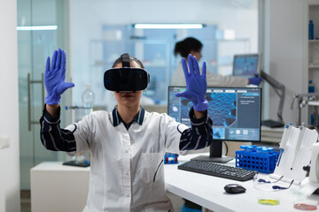 Biologist researcher wearing virtual reality headset examining biochemistry experiment working in microbiology hospital laboratory using biotechnology. Specialist scientist analyzing virus development