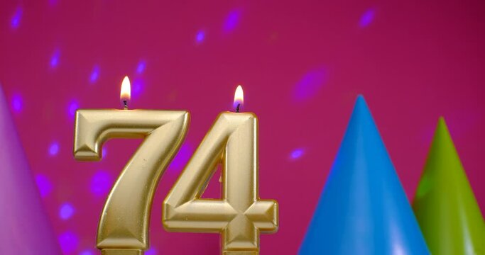 Burning birthday cake candle number 74. Happy Birthday background anniversary celebration concept. Birthday hat in the background