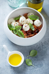Caprese salad with mini mozzarella balls, red cherry tomatoes and fresh green basil, vertical shot on a light-blue stone background