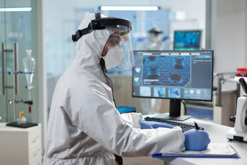 Biologist man doctor writing medical treatment against covid19 during clinical investigation in microbiological hospital laboratory. Biologist researcher wearing protective equipment against virus