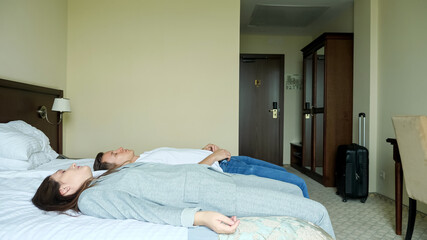 tired young couple of man and woman with a suitcase enters the hotel room and fall on the bed.