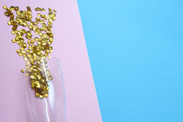 Glass of champagne with loose sparkles on a pink blue background and place for text. Holiday and celebration concept. New Year. Copy space.