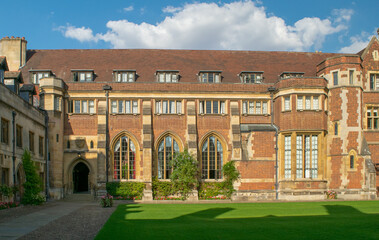 Facade of Historical bricked building with ornate entrance and medieval windows in front of lawn at Cambridge England