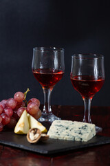 Wine, cheese, some grapes and pear on wooden plate on black background