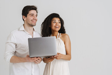 Multiracial excited couple posing with laptop and smiling