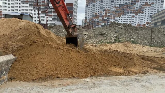 The excavator's orange bucket picks up sand from a large pile of sand. 