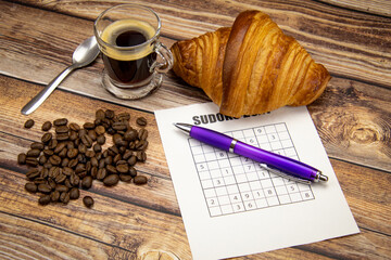 feuille de sudoku sur une table avec un café et croissant