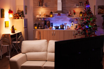 Empty xmas living room with nobody in it ready for winter holiday at home. In background x-mas decorated kitchen with modern furniture. Christmas decorations at home. Christmas festive ornaments