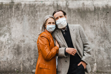 White senior couple in face masks hugging and looking at camera